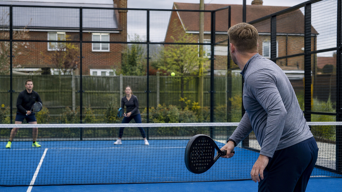 Padel court beside a residential boundary with glass walls and players mid-rally