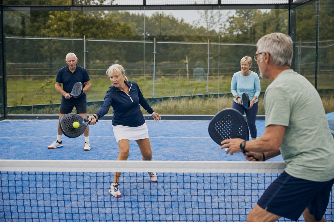 Four older adults enjoying a friendly doubles padel game on an outdoor court